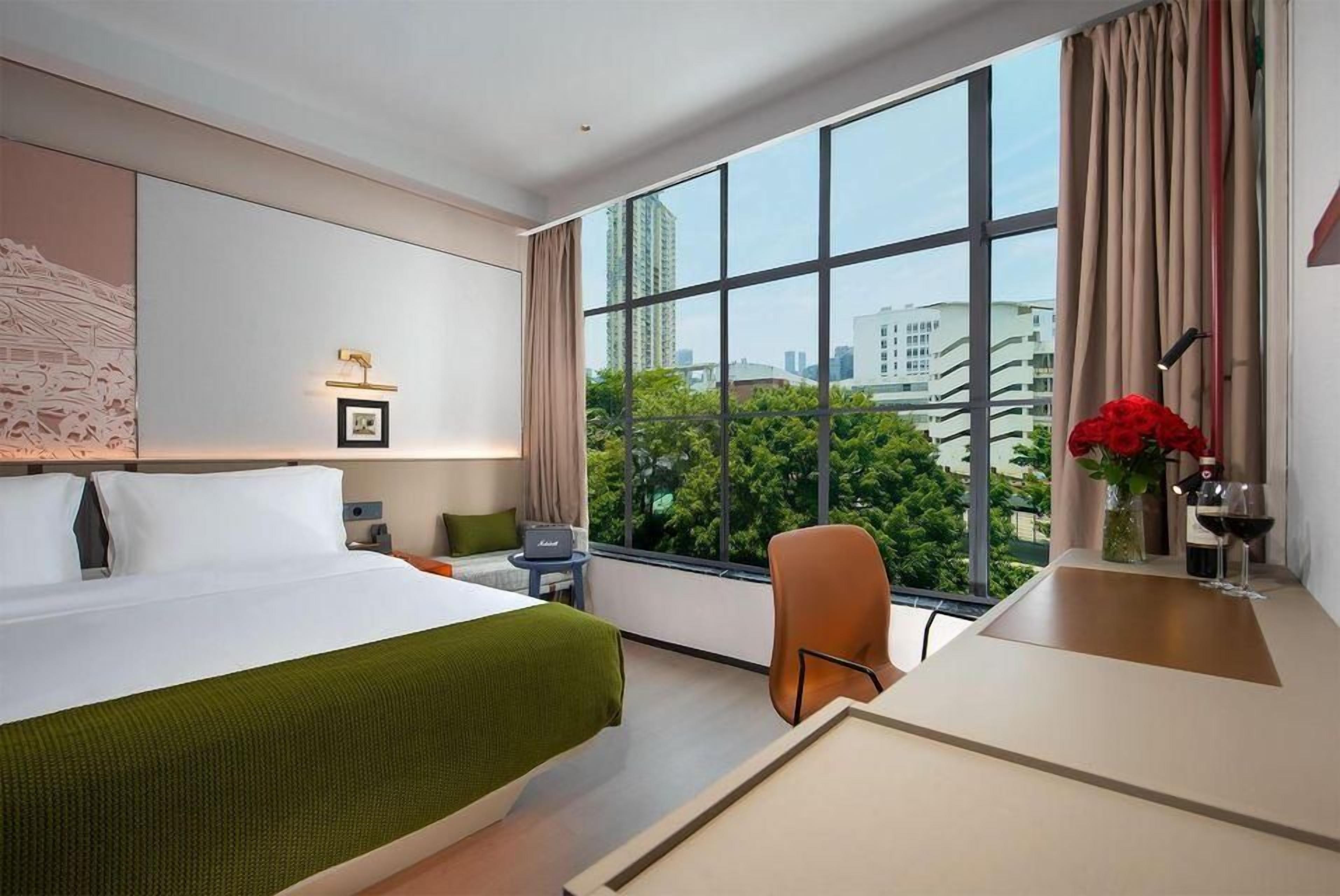 A hotel room with a large window, a bed, a desk, and a chair.