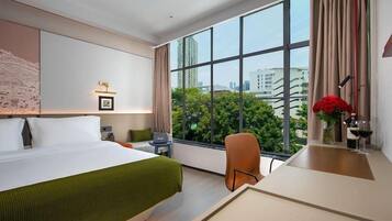 A hotel room with a large window, a bed, a desk, and a chair.