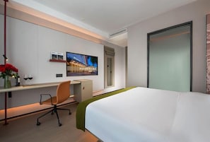 Una habitación de hotel con una cama, un escritorio, una silla, un televisor y una puerta.