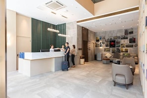 A hotel lobby with a reception desk, seating area, and a wall with various photographs. - Aite Community Hotel (Beijing)