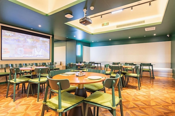 A conference room with multiple tables and chairs, a large screen for presentations, and a projector. - Aite Community Hotel (Beijing)