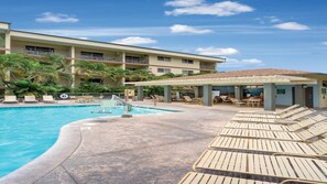 Ett hotell med en swimmingpool, solstolar och ett takförsett område med bord och stolar.
