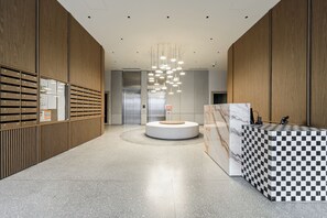 A modern lobby with a checkered marble reception desk, a central seating area, and a row of lockers on the left. - Lumina 2 rooms apart I Warsaw center (Warszawa)