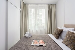 A hotel room with a bed, a window with curtains, a rolled towel, and a magazine on the bed. - Lumina 2 rooms apart I Warsaw center (Warszawa)