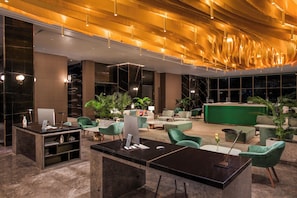 A modern lobby with a reception desk, seating area, and large windows. - Voco Muscat Al Mouj (Muscat)