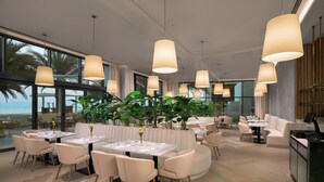 Un comedor moderno con mesas, sillas y lámparas colgantes.