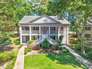 A two-story building with a front porch, a staircase leading to the entrance, and a flagpole with an American flag. - Par For Pawleys, Golf, Pool & Near the Beach (Pawleys Island)