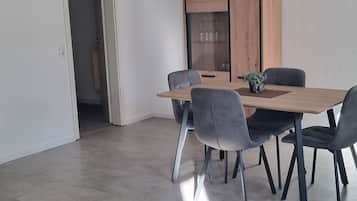 Ein Essbereich mit Holztisch und grau gepolsterten Stühlen, einem Holzschrank mit Glastüren und einer Deckenleuchte.