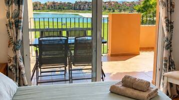 A hotel room with a bed, a view of a golf course, and a balcony with a table and chairs.