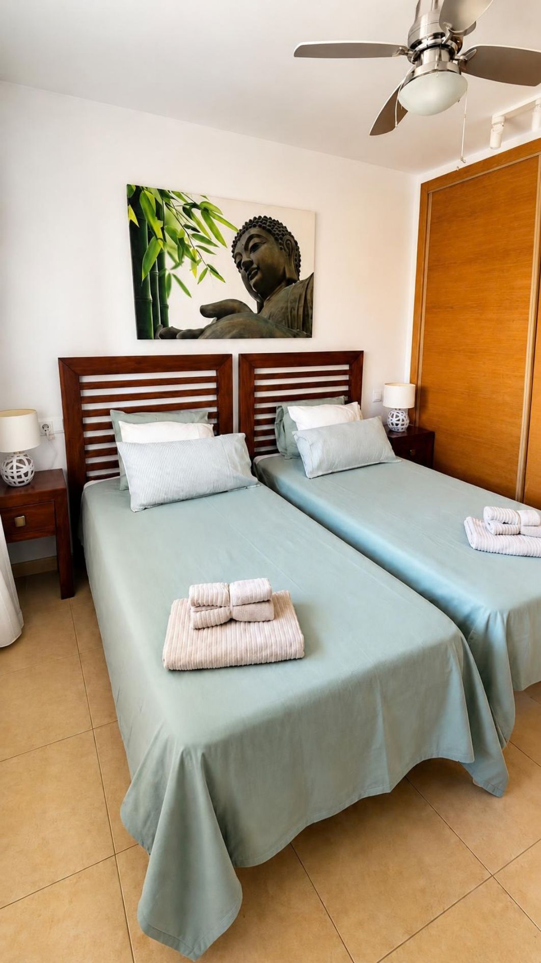 Habitación de hotel con dos camas, ventilador de techo, una estatua de Buda montada en la pared y un armario de madera.