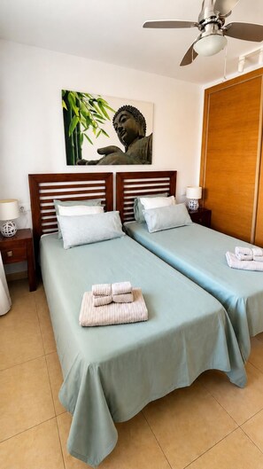 A hotel room with two beds, a ceiling fan, a wall-mounted Buddha statue, and a wooden wardrobe.