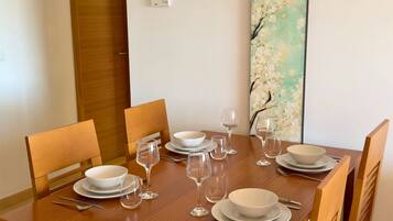 Una mesa de comedor dispuesta con platos, tazones y copas de vino, rodeada de sillas de madera.
