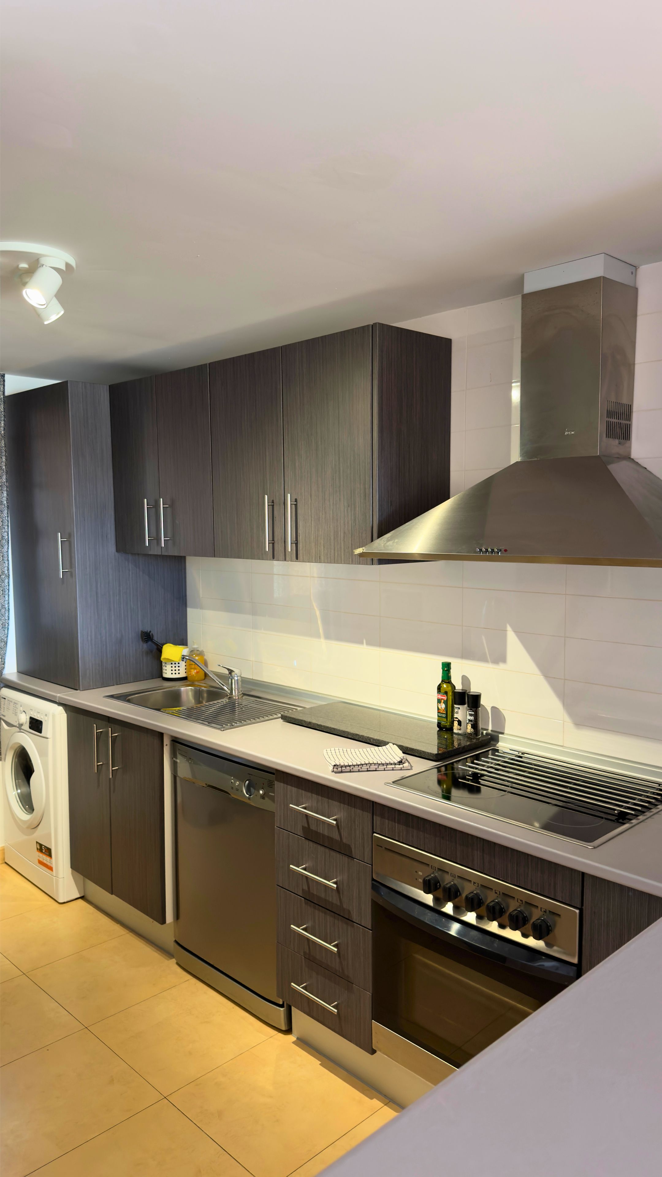 Una cucina moderna con mobili in legno scuro, una cappa aspirante in acciaio inossidabile, un forno integrato e una lavastoviglie.