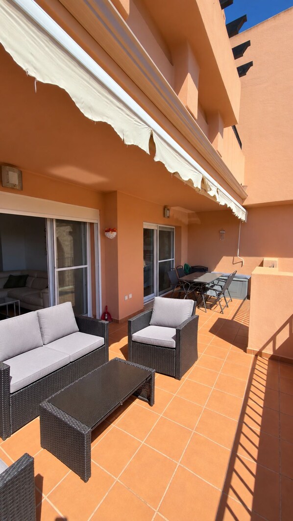 An outdoor patio with wicker furniture, a table, and a covered area with a white awning.