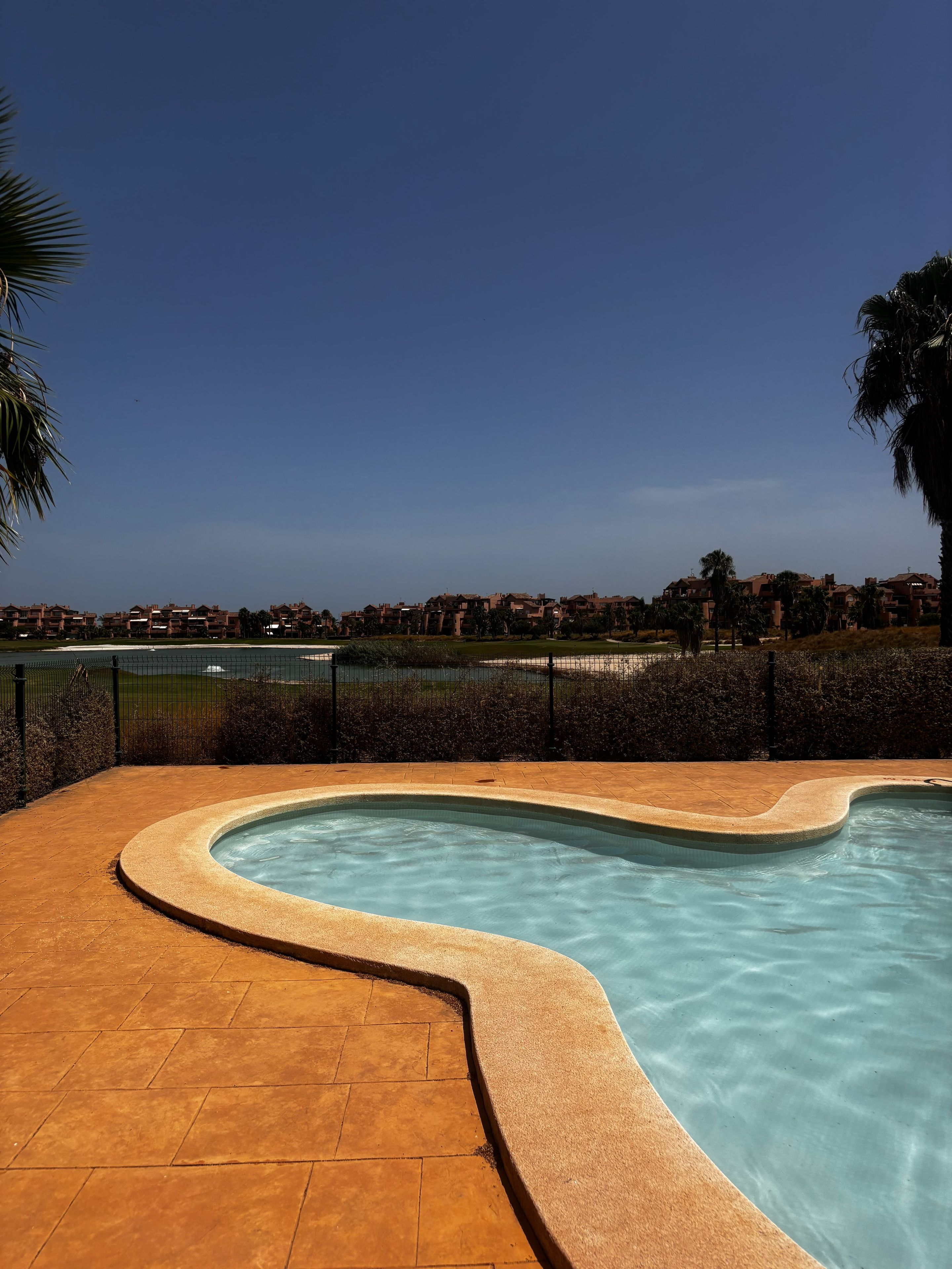 Una piscina con borde curvo, rodeada por un patio de ladrillo.