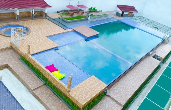 Una piscina con un deck perimetral, un pequeño jardín y una cancha de tenis.