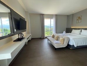Habitación de hotel moderna con una cama grande, un sofá, un televisor y vistas al exterior.