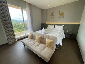 Habitación de hotel con una cama grande, un sofá y vistas a la vegetación a través de la ventana.
