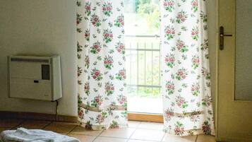 Une chambre avec un lit, un radiateur et une porte donnant sur un balcon équipé de rideaux.