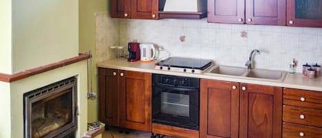Een keuken met houten kastjes, een fornuis, een spoelbak en een open haard.