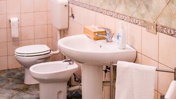 Un baño con inodoro, bidé, lavamanos y un perchero para toallas.