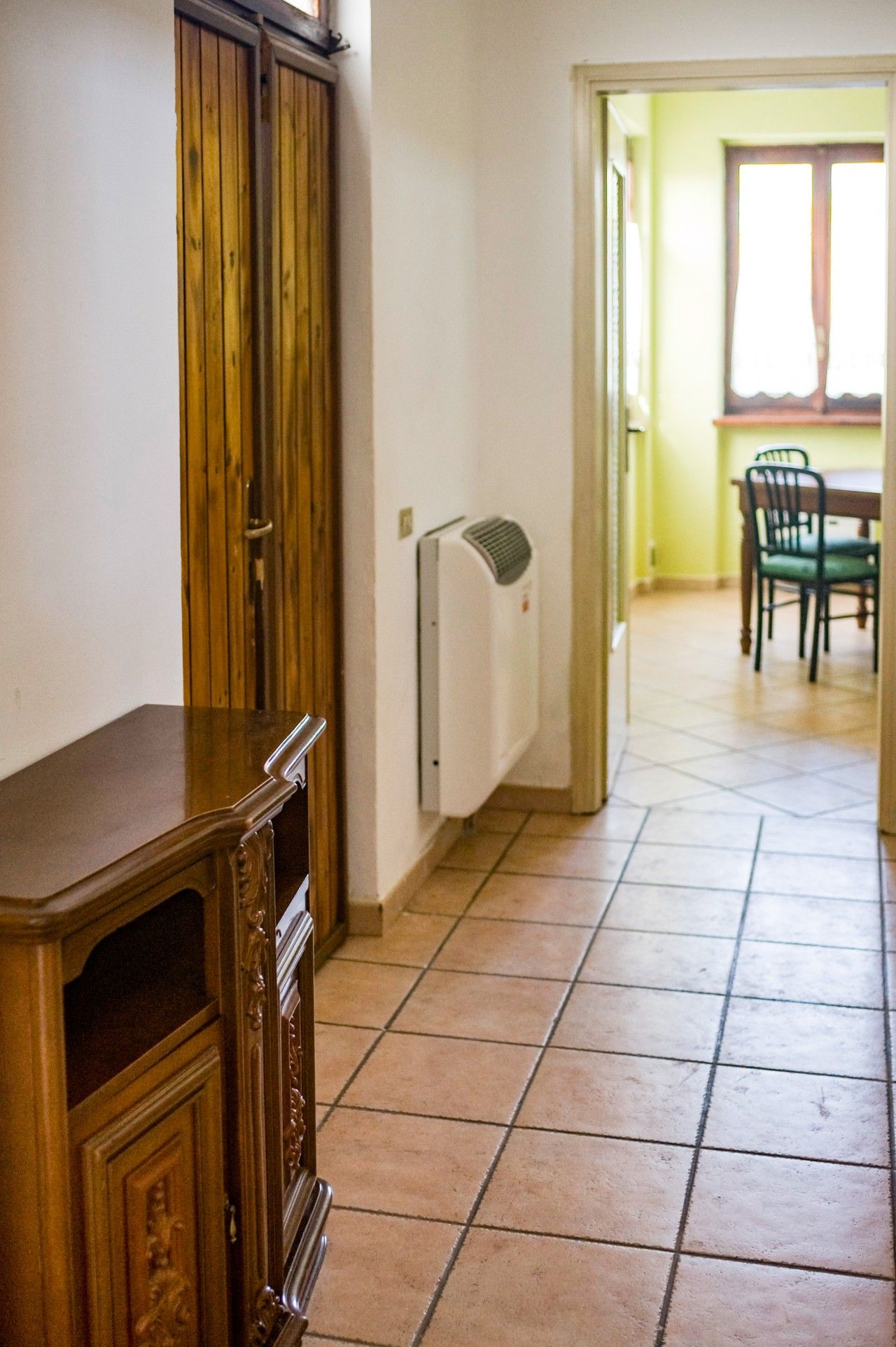 A hallway with a wooden cabinet, a white radiator, and a dining area with chairs and a table.
