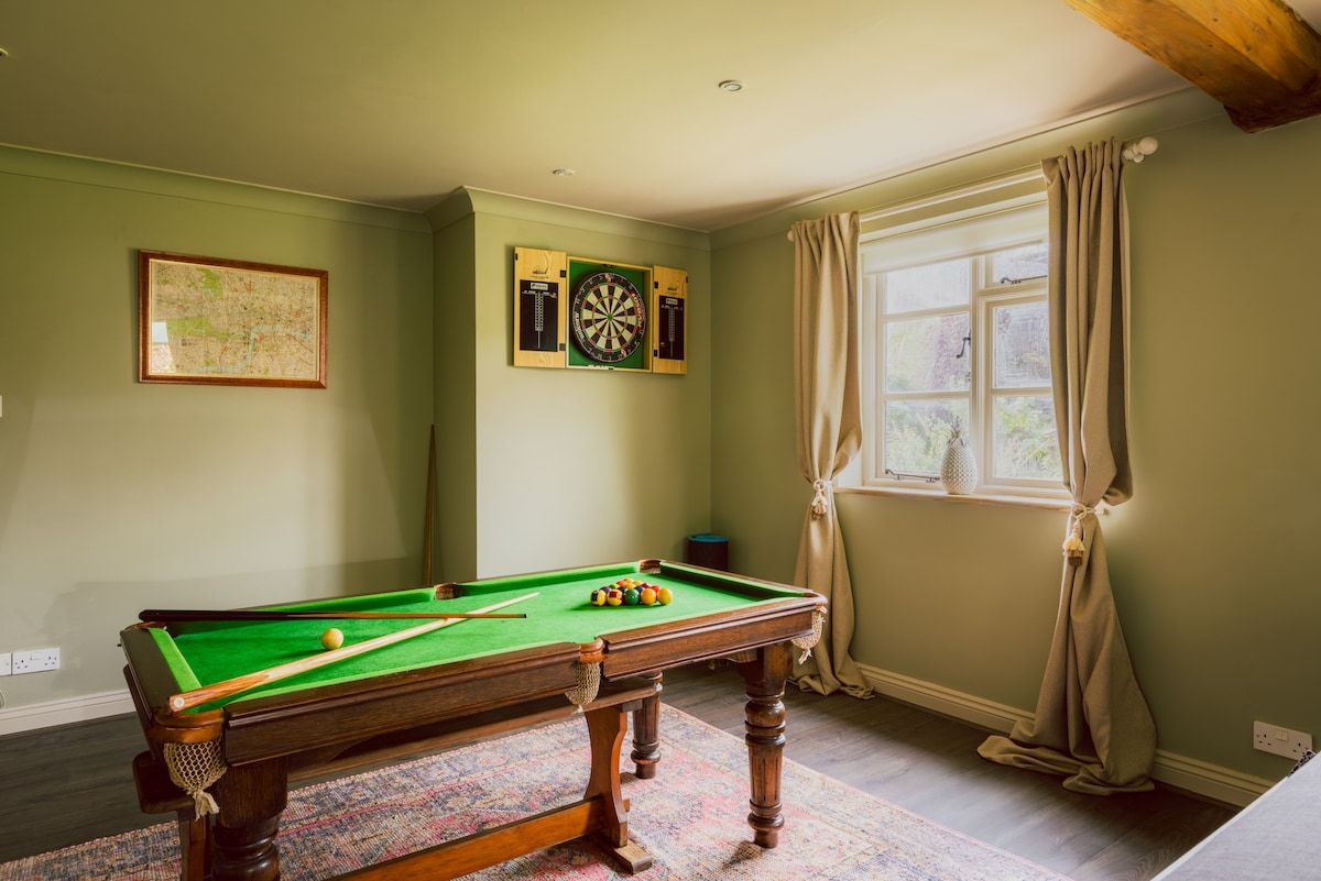 Een pooltafel met ballen, een dartbord en een inlijste kaart aan de muur.