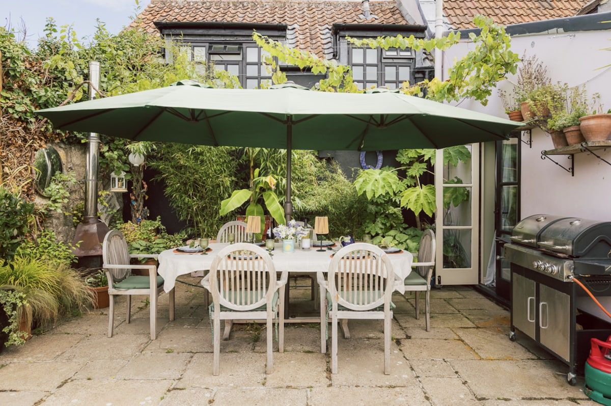An outdoor patio with a table and chairs, a grill, and potted plants.