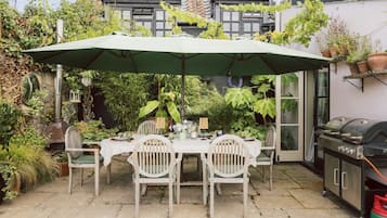 An outdoor patio with a table and chairs, a grill, and potted plants.