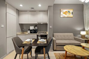 A modern kitchen with a dining area, a sofa, and a small table. - Near Metro  1BR  Pool view & Prime Location (Dubai)