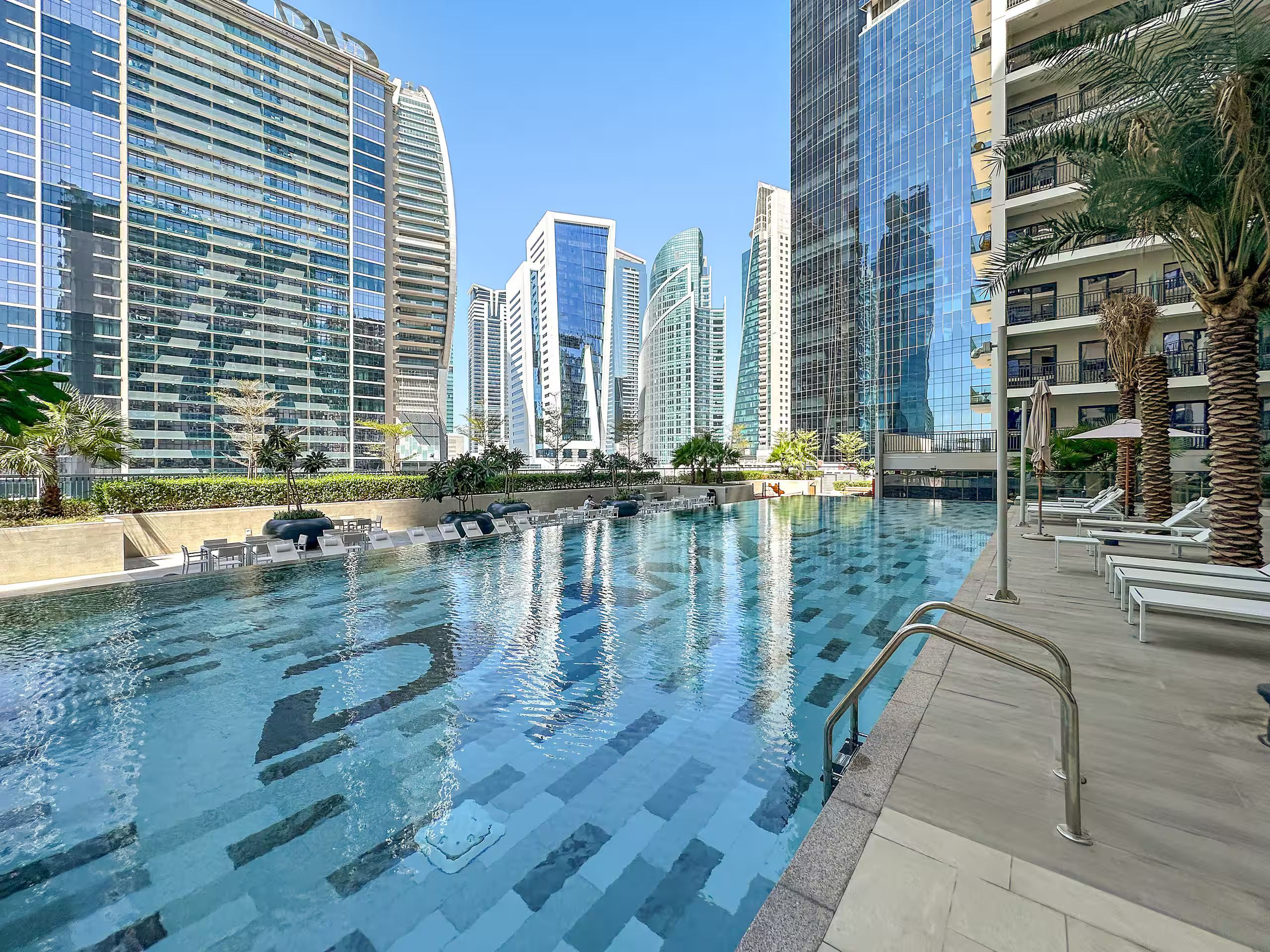 Una piscina con sillones de descanso y vistas a modernos edificios altos.