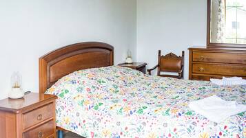 Un dormitorio con cama de madera, una mesita de noche, una silla, un aparador y un espejo.