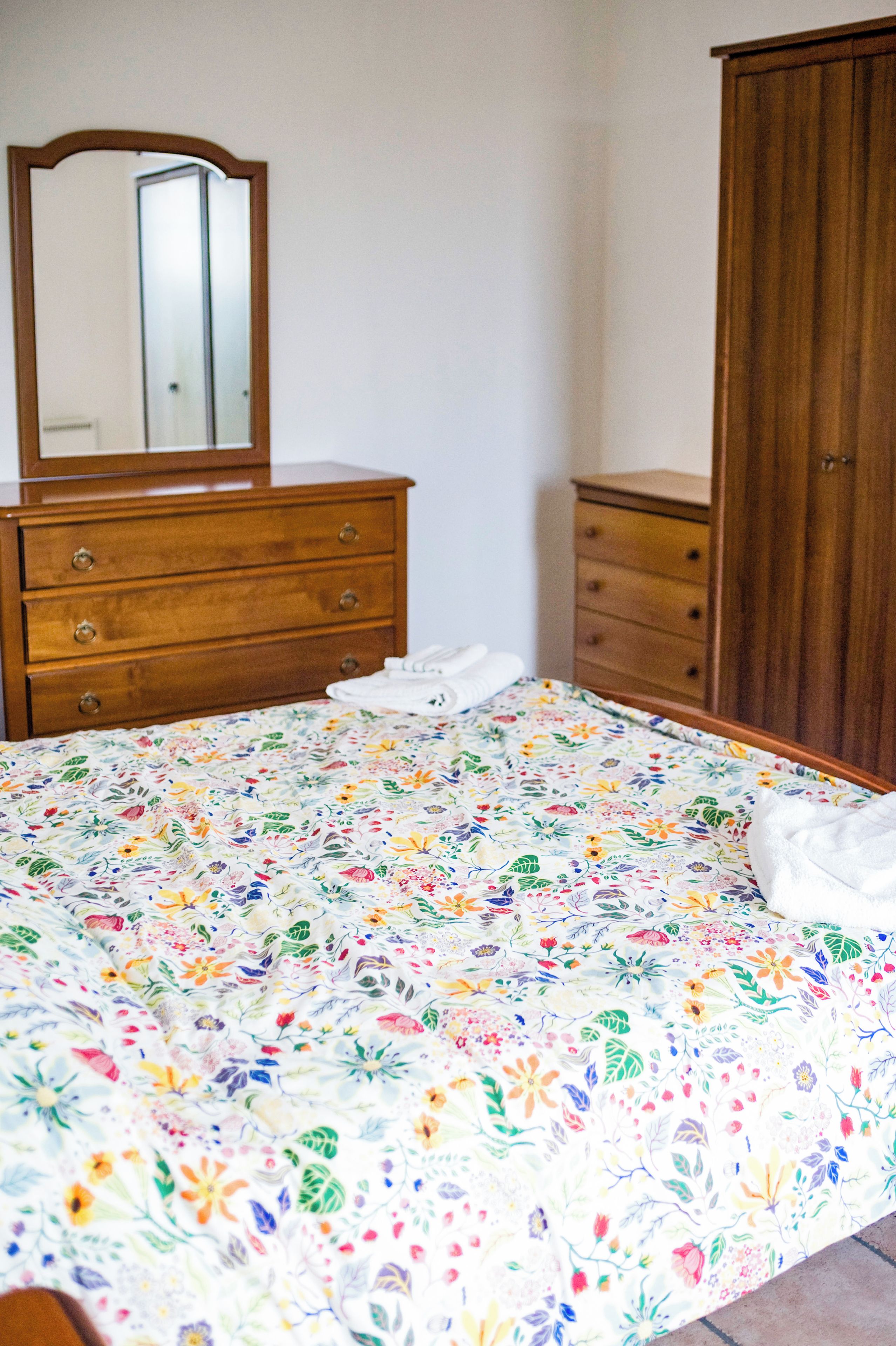 A bedroom with a bed, a dresser, a wardrobe, and a mirror.