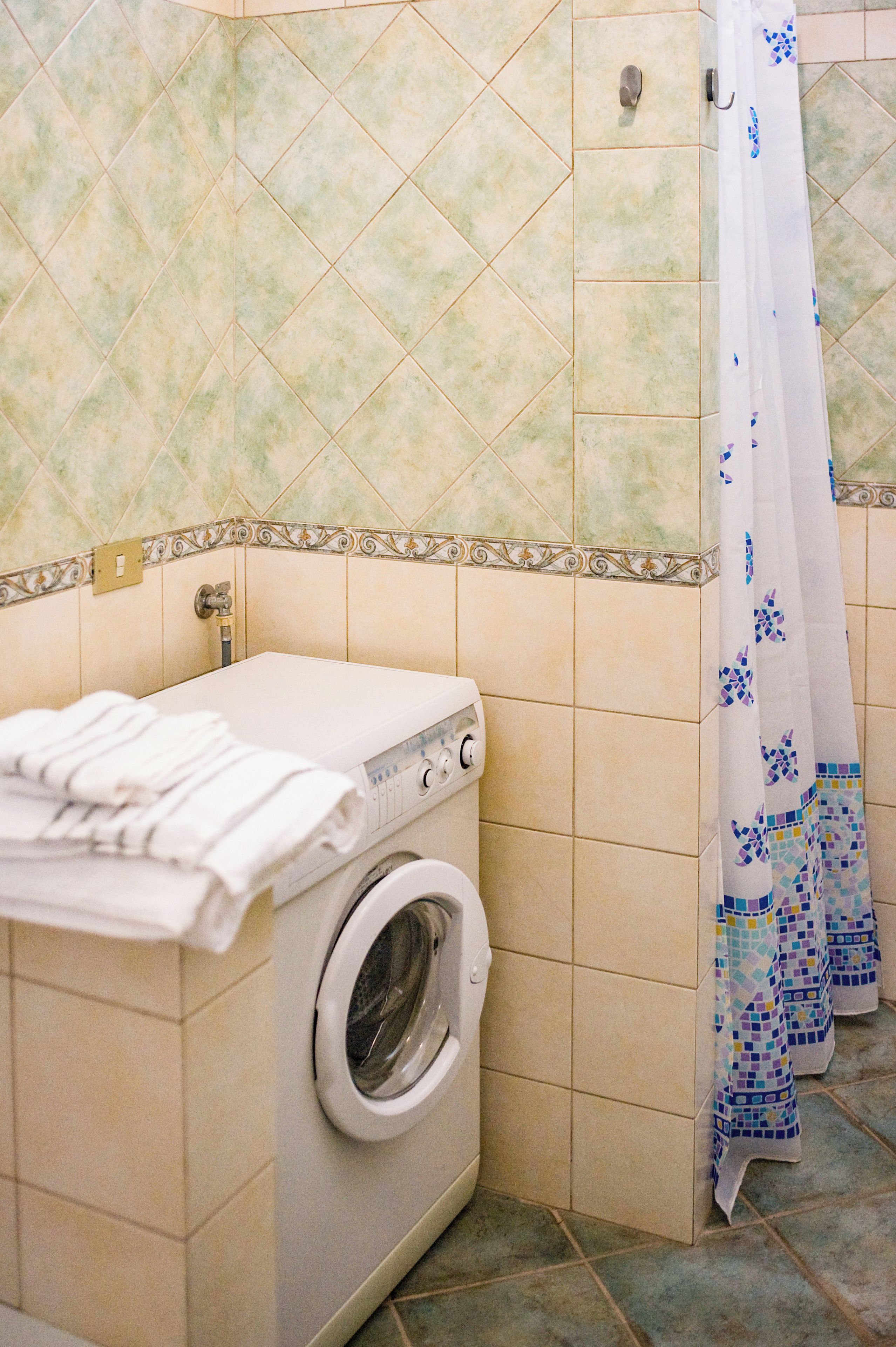 A laundry area with a washing machine, a towel rack, and a shower curtain.