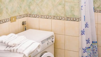 A laundry area with a washing machine, a towel rack, and a shower curtain.