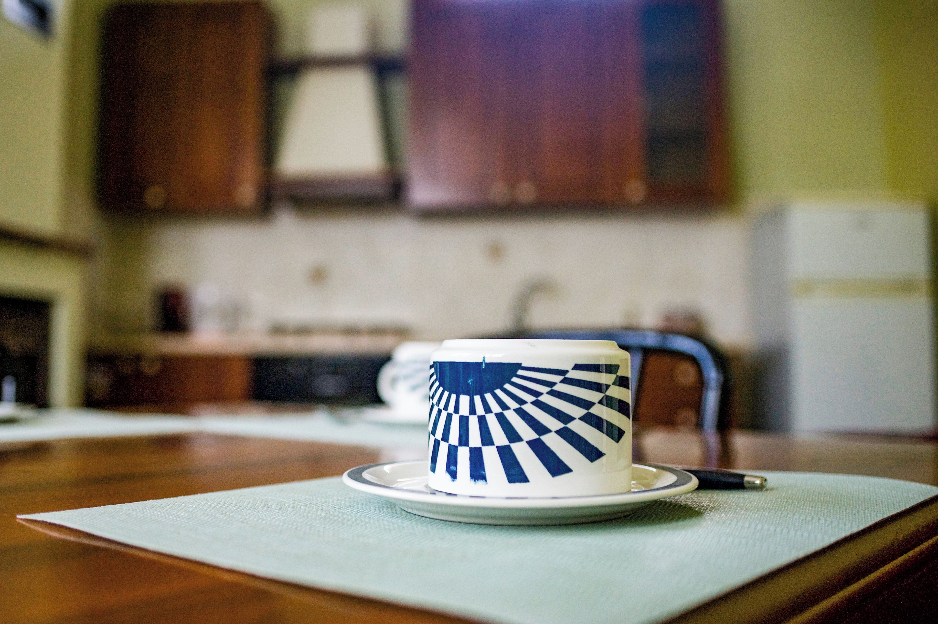 Una taza con un diseño azul y blanco sobre un platito, colocada sobre una mesa con un posavasos.