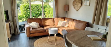 Una sala moderna con un sofá de cuero marrón, una mesa de comedor redonda de madera y un ventanal con cortinas.