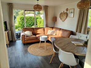 Ein modernes Wohnzimmer mit einer braunen Ledersofa, einem runden Holzesstisch und einem großen Fenster mit Vorhängen.