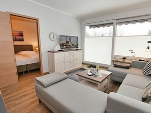 Ein modernes Wohnzimmer mit einer Couch, einem Couchtisch, einem Fernseher und einem Bett mit Blick nach draußen.