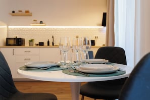 Ett matbord dukat med tallrikar, glas och bestick, med en mikrovågsugn och köksredskap i bakgrunden.