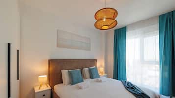 Ett hotellrum med en säng, sänglampor, en sänggavel, ett fönster med gardiner och ett konstverk som hänger på väggen.