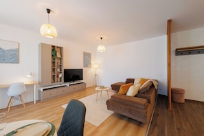 Ett modernt vardagsrum med en platt-TV, en soffa, ett soffbord och en matplats med en stol och ett bord.