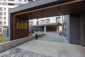 Ein moderner Gebäudeeingang mit einem großen 'M8'-Schild, einer überdachten Außenbereichssitzgelegenheit und einem gepflasterten Innenhof.