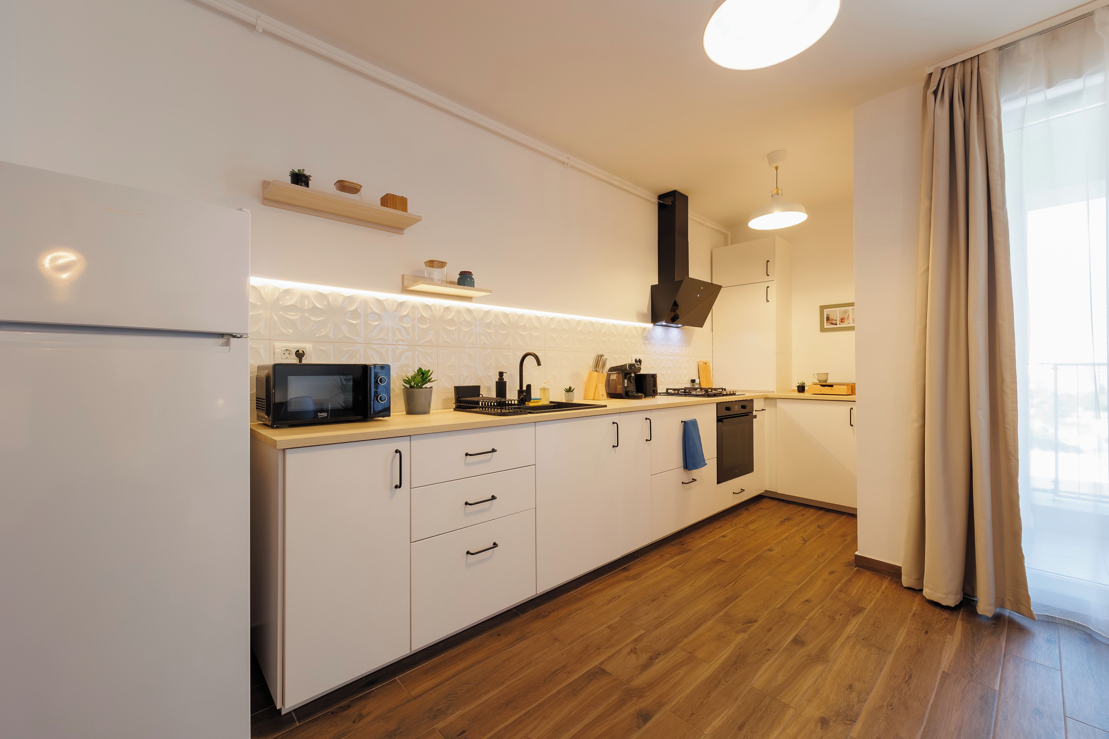 Une cuisine moderne avec des meubles blancs, un four à micro-ondes, une cuisinière et un évier.