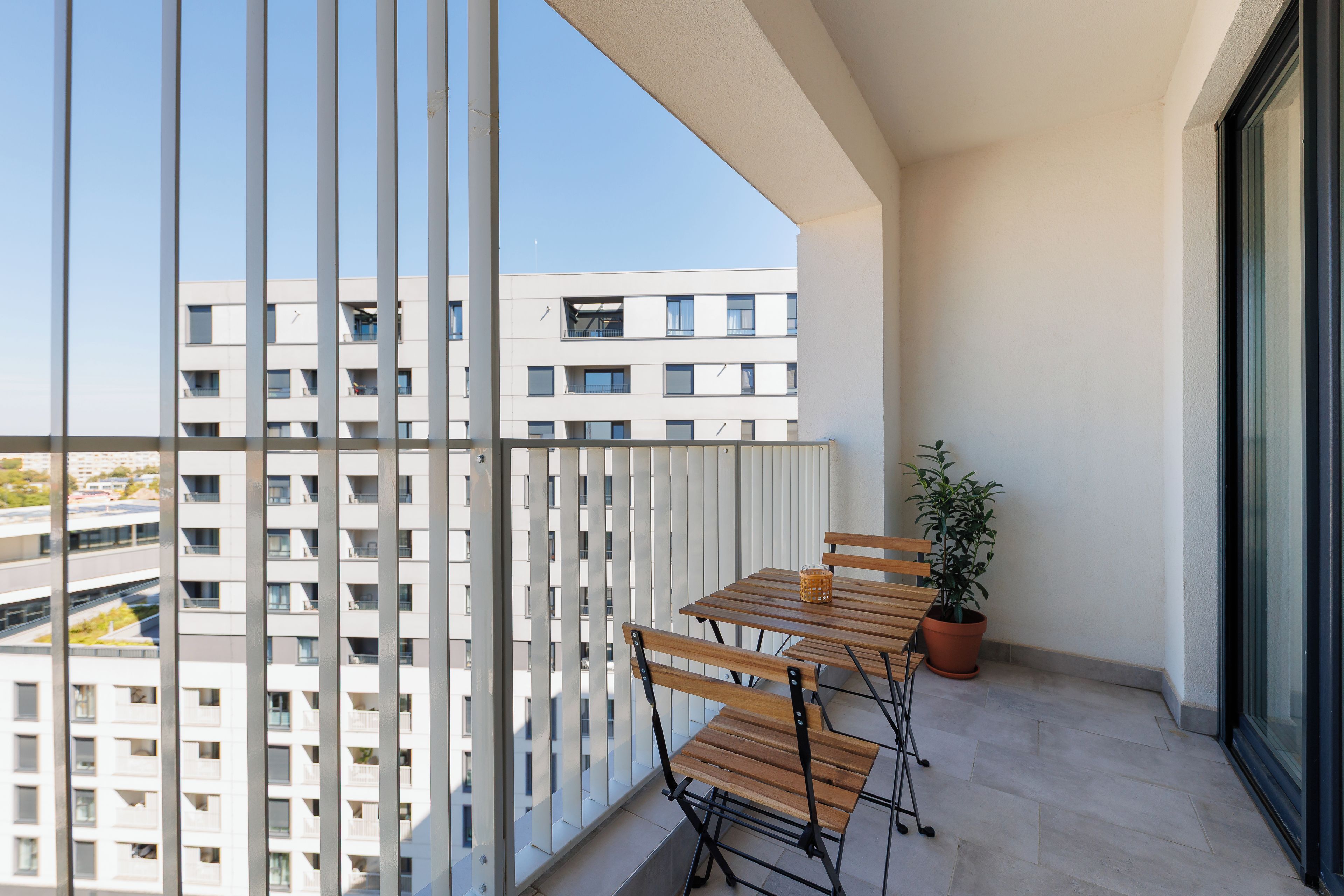 A balcony with a table and chairs, a potted plant, and a view of a building.