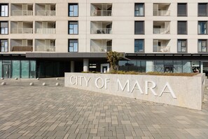 Ein mehrstöckiges Gebäude mit Balkonen, einem Schild mit der Aufschrift 'CITY OF MARA' und einem gepflasterten Eingangsbereich.