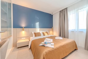 Ein modernes Hotelzimmer mit einem großen Bett, Nachttischen, einer Leseecke und Blick ins Freie.