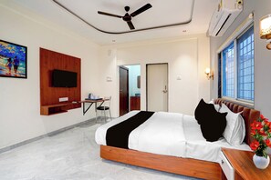 A modern hotel room with a bed, a desk, a flat-screen TV mounted on the wall, and a window with a view. - Townhouse Chakan Corporate Homestay (Rajgurunagar)