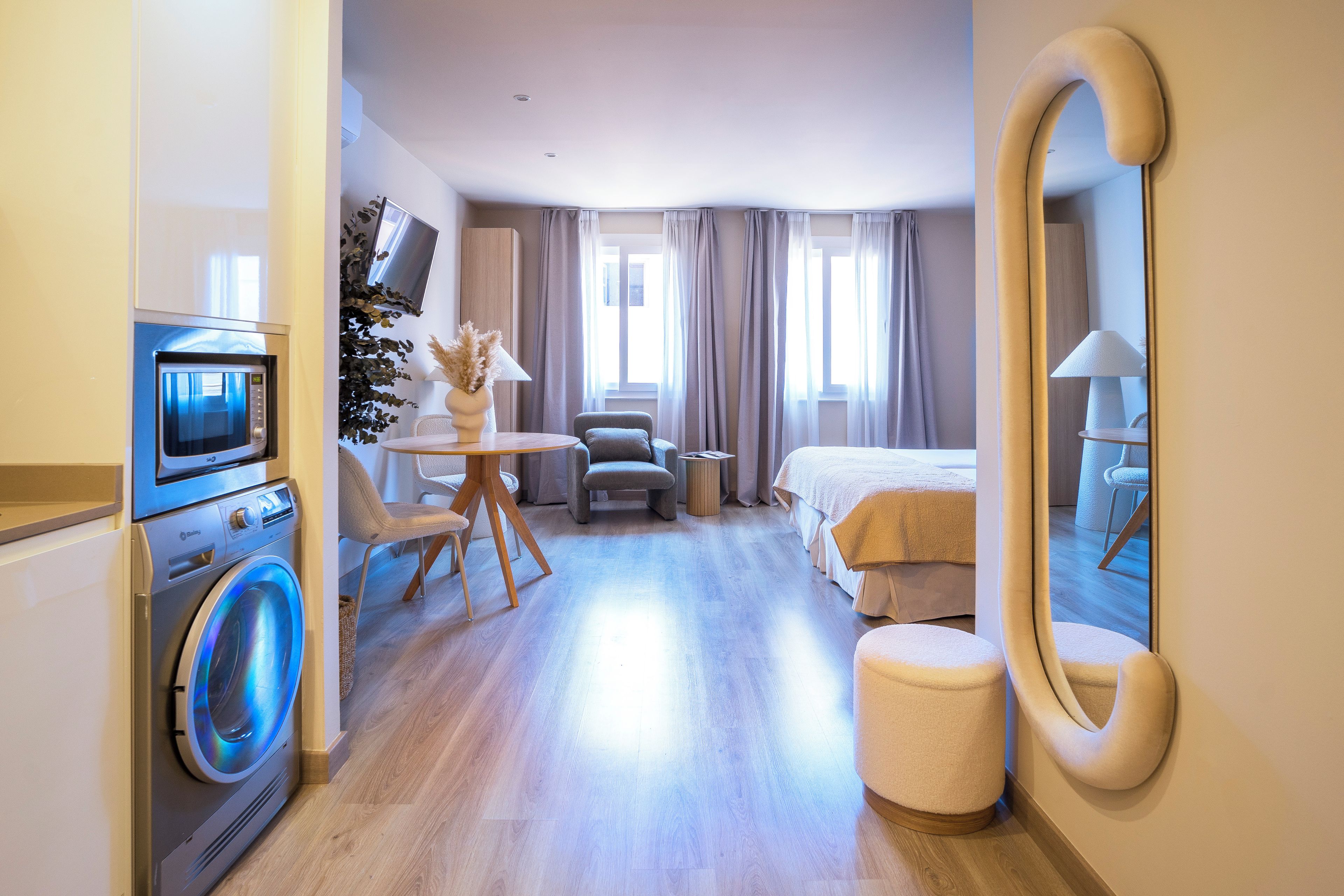 Une chambre d’hôtel équipée d’un lave-linge, d’un lit, d’une chaise, d’une table avec une lampe et d’un grand miroir.