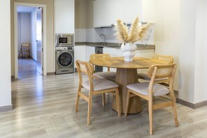 A dining area with a round wooden table and four chairs, a washing machine, and a microwave in the background. - Housing Atarazanas by Sharingco (Málaga)